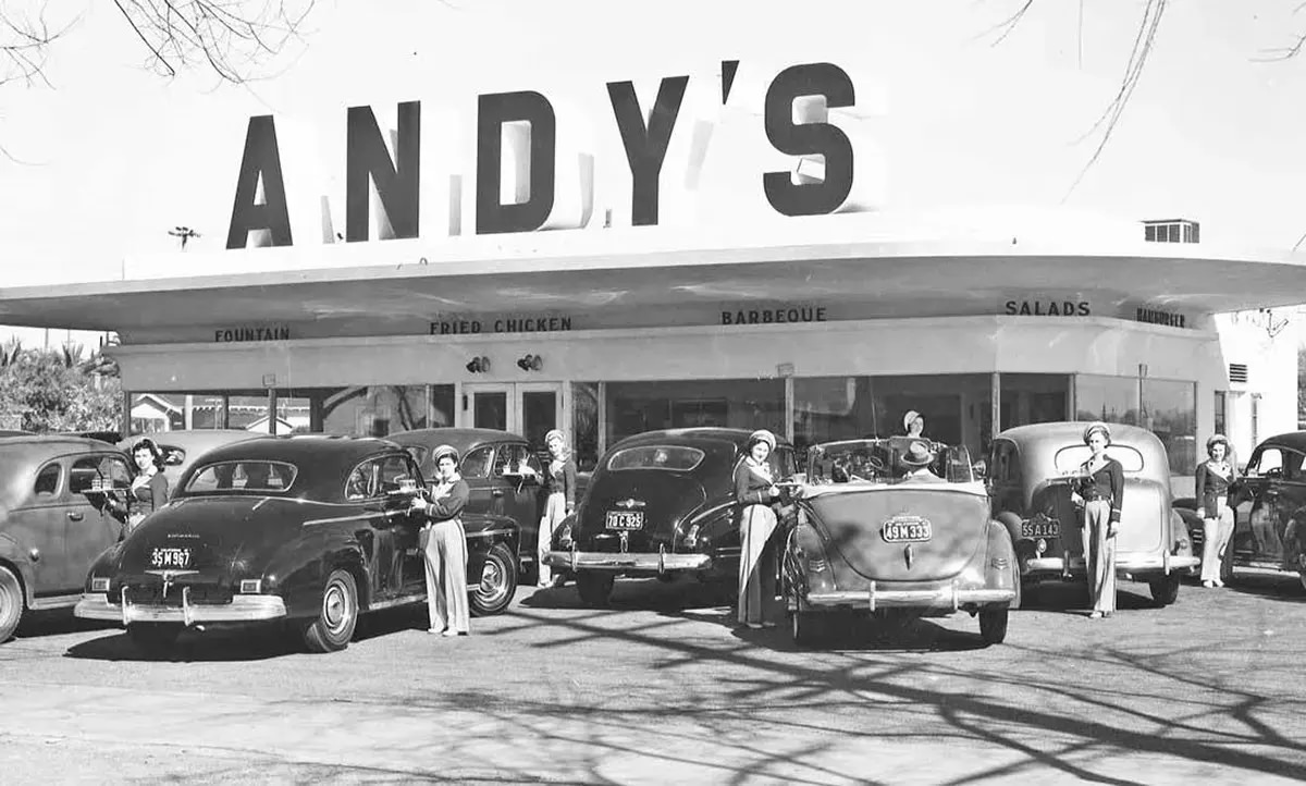 Andy’s Drive-In with carhops pose in front with cars they’re serving, 1941.