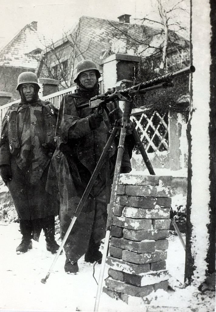 German machine gunners muffled to the ears against the severe cold stand ready for action in a Prague street.