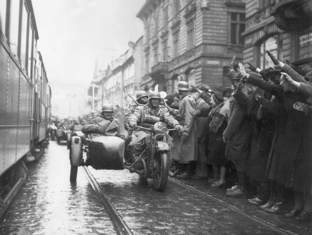 Crowds on the sidewalk salute Nazi soldiers riding in a motorcycle infantry unit as German troops enter Prague, Czechoslovakia.
