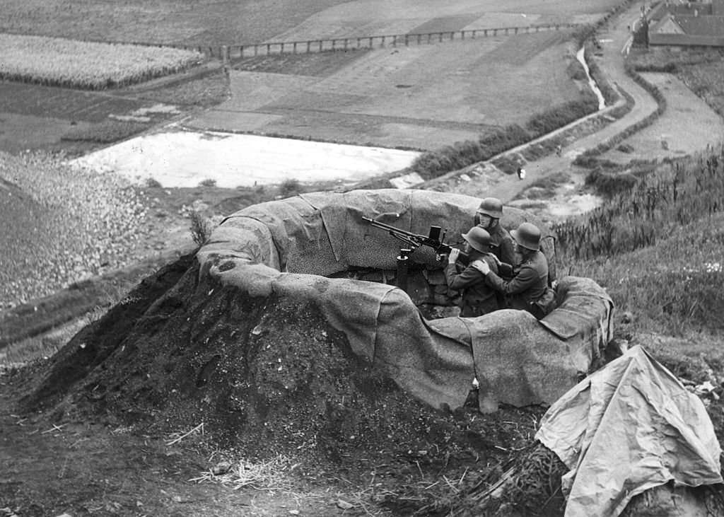 Three German soldiers sit behind an anti-aircraft machine in a camouflaged post overlooking the Sudetenland countryside, Czechoslovakia, World War II.
