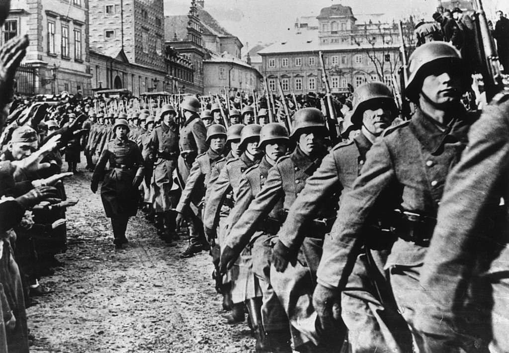 Steel helmeted German troops marching into Prague during the invasion of Czechoslovakia. By-standers are giving them a German salute.