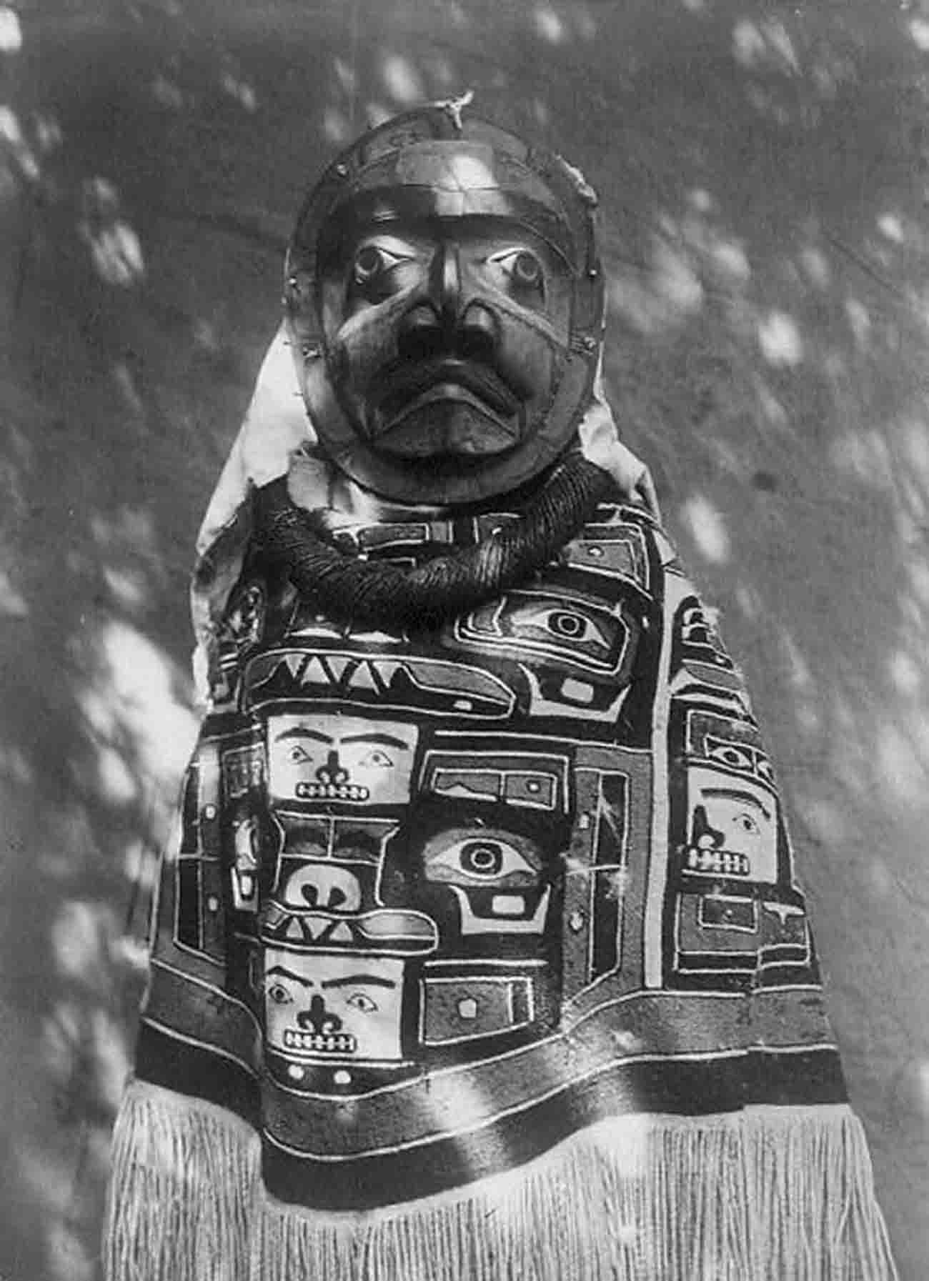 Woman wearing a fringed Chilkat blanket, a hamatsa neckring, and a mask representing a deceased relative who had been a shaman.
