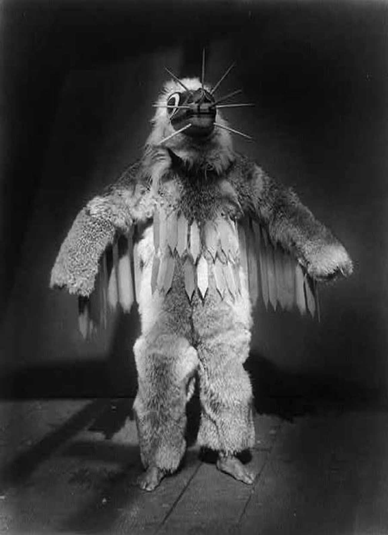 Ceremonial dancer, full-length portrait, standing, wearing mask and fur garments during the Winter Dance ceremony.