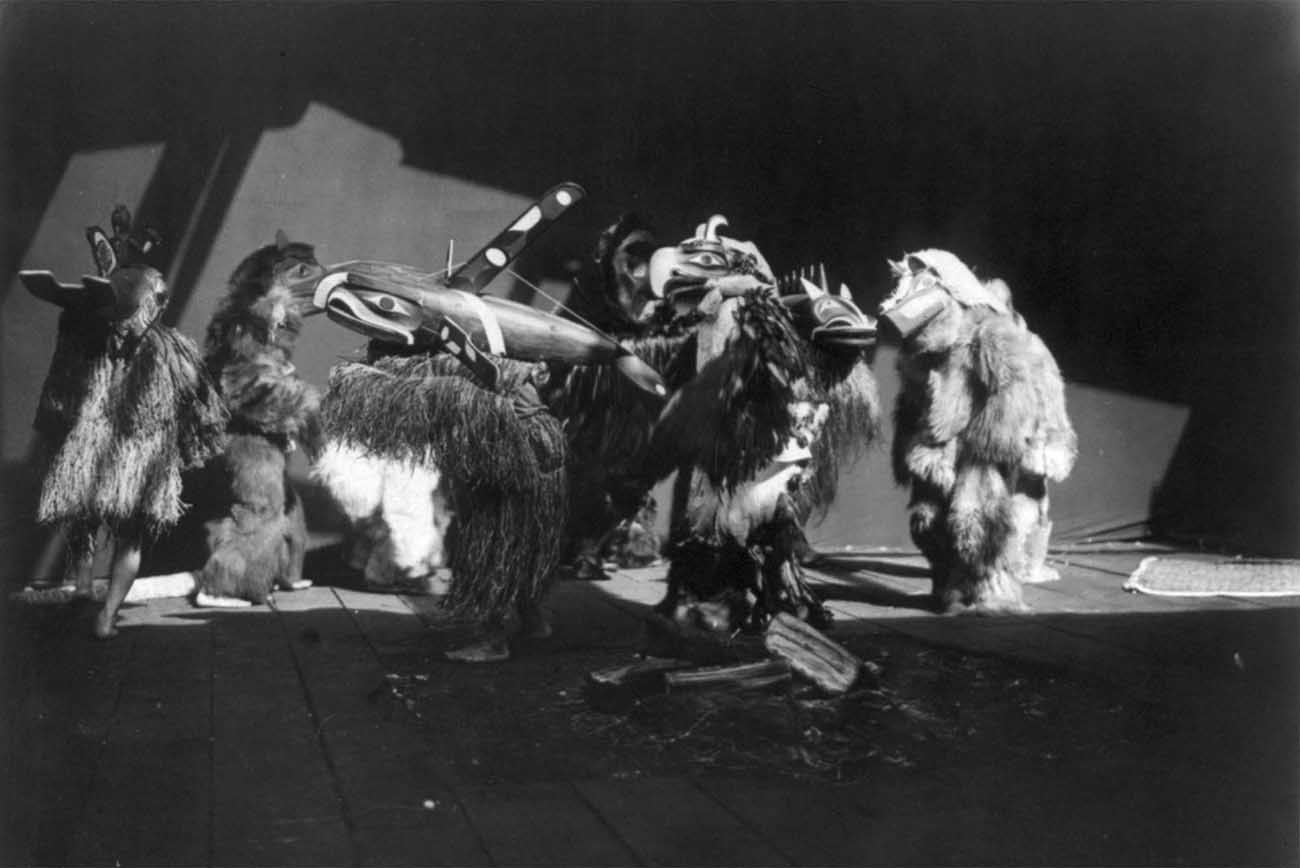Ceremonial dancers, in a circle during the Winter Dance ceremony, wearing masks and garments of fur, feathers, and other materials.