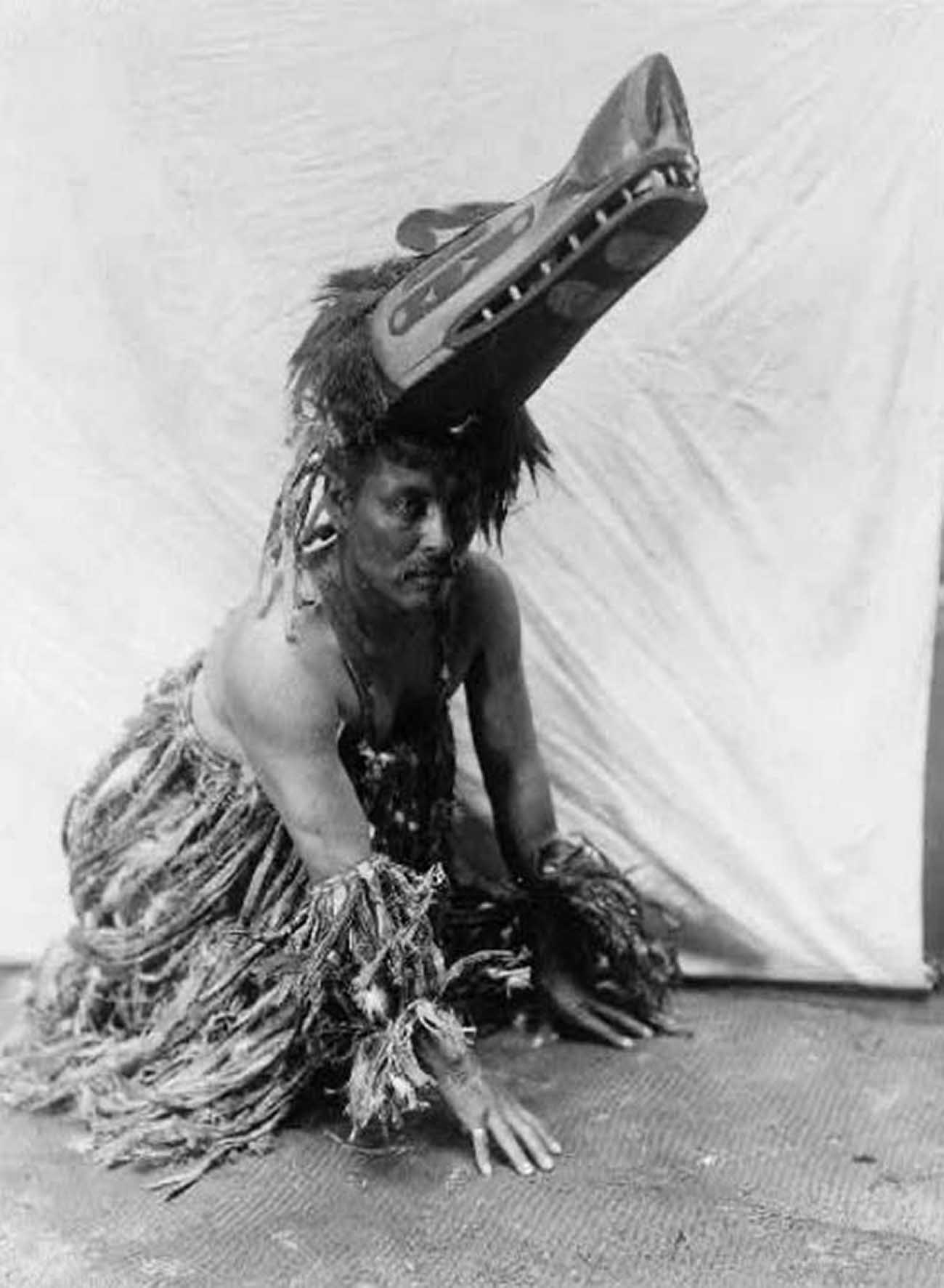 Koskimo man in costume with ceremonial mask, on hands and knees.