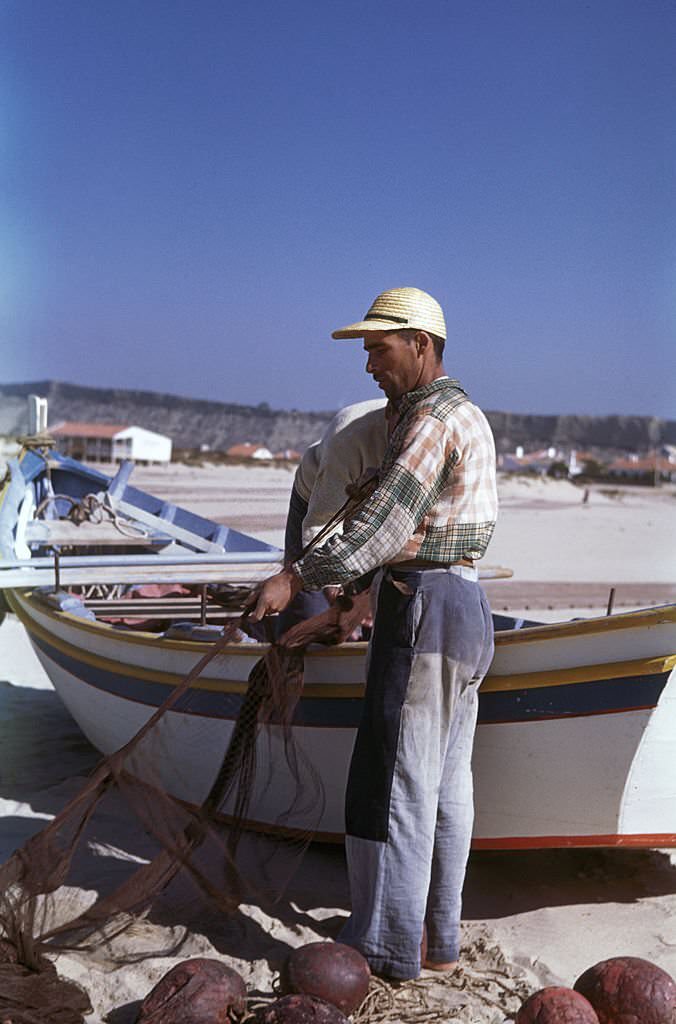 Portuguese fishermen prepare their nets on the beach at Nazare, 1955.