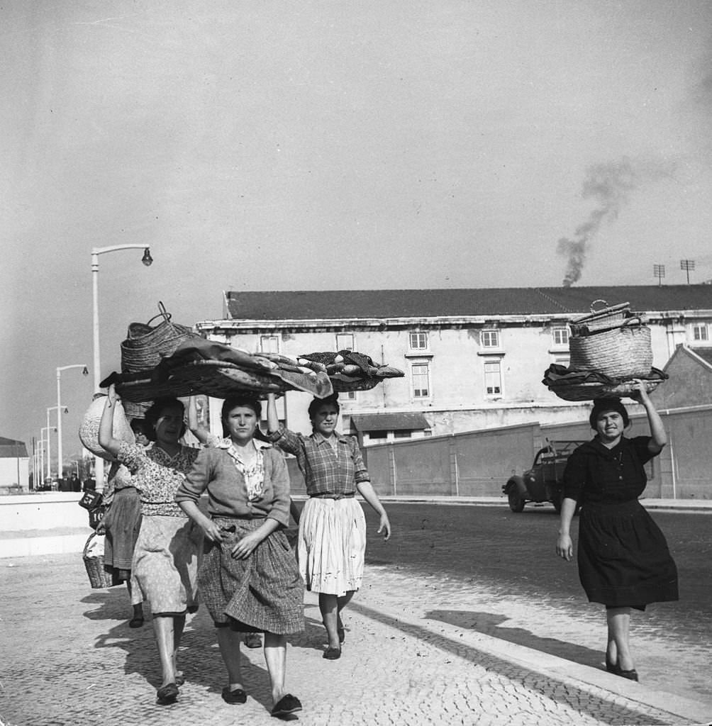 Portuguese fisherwomen, known as 'varinas', walk along the docks on the Tejo River carrying empty baskets which they use to take fish to market, 1955