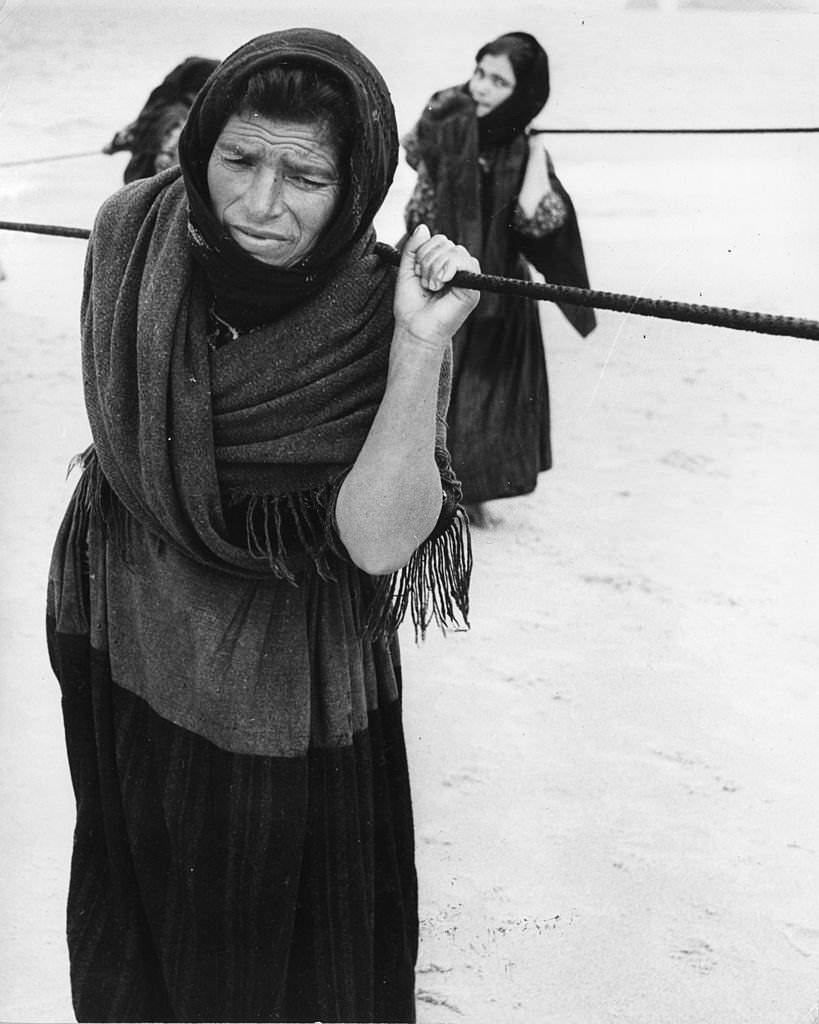 Women pulling in fishing boats at Nazare, Portugal.