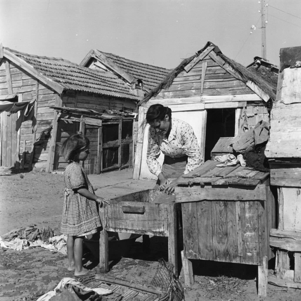 A woman washes clothing in a wooden container in a Portuguese fishing village.