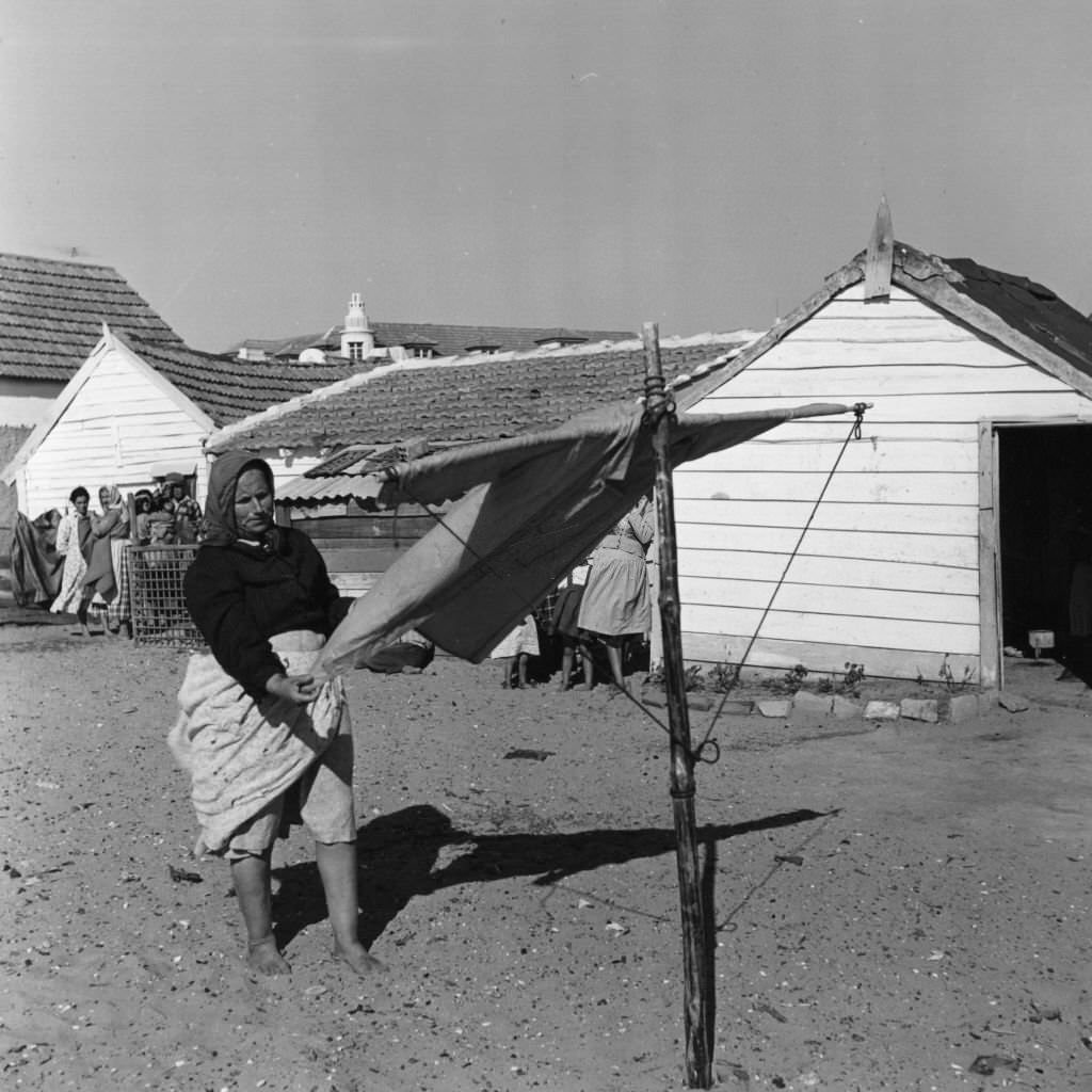 A woman in a Portuguese fishing village hangs out a dress to dry while her neighbours watch.