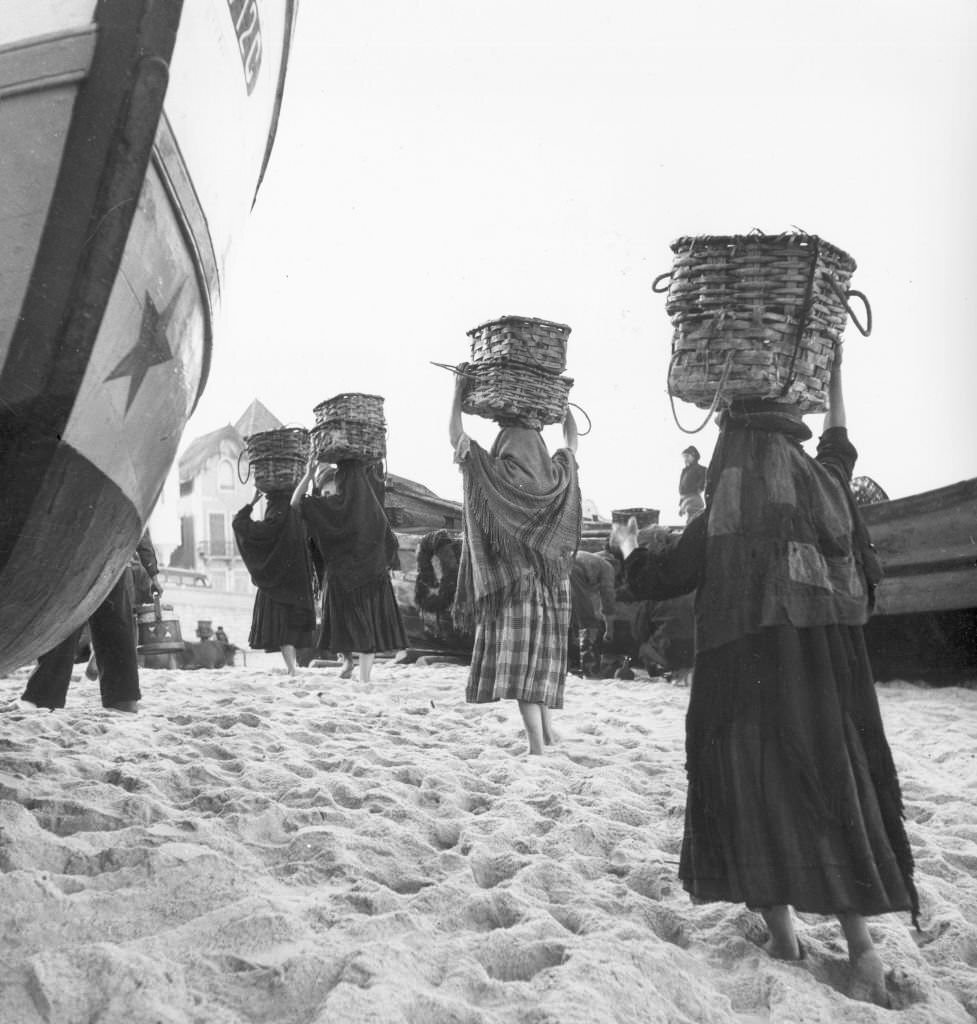 Women carrying fish in baskets on the beach at Nazare.