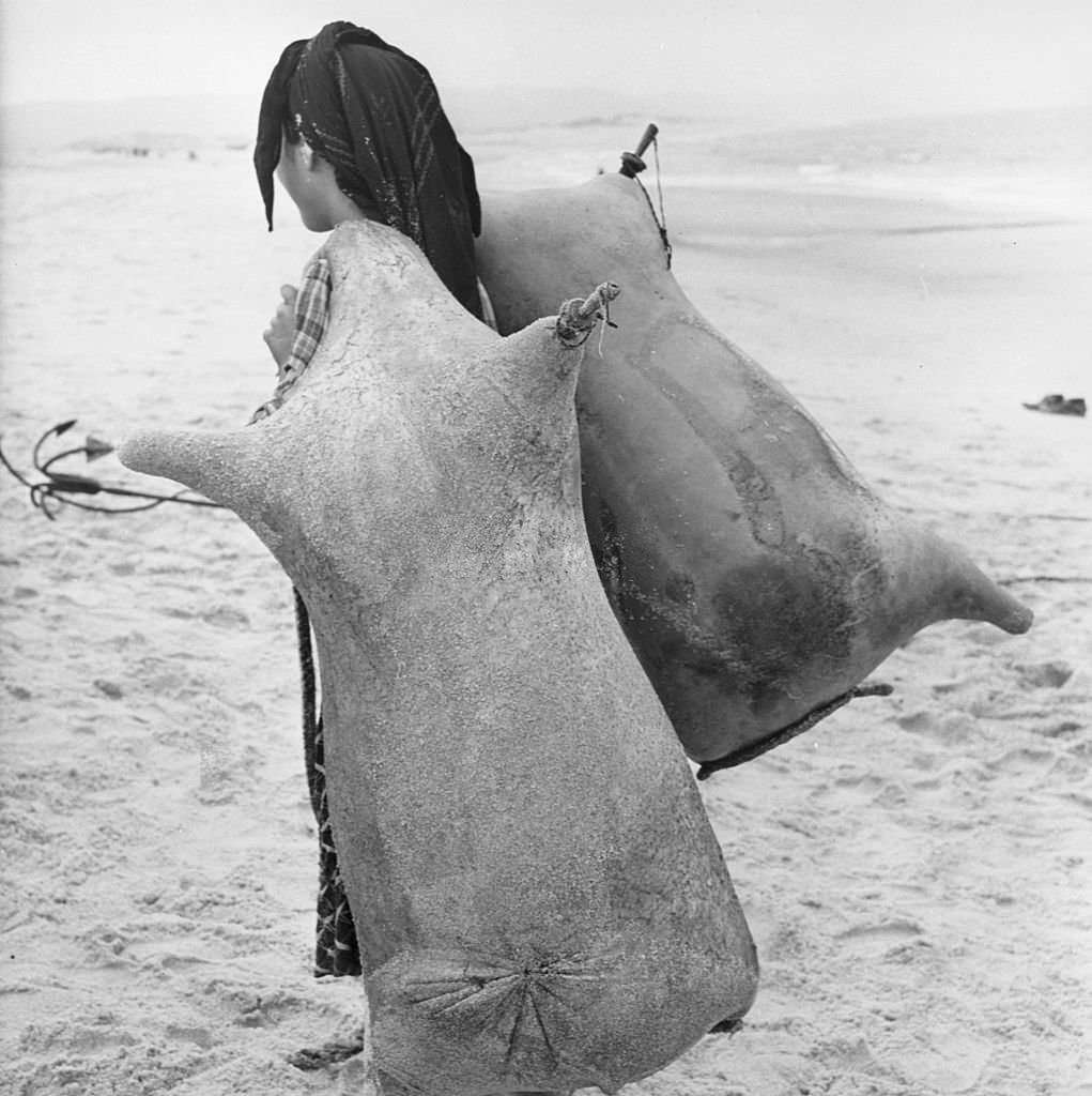 A girl carrying two animal skins full of water in the Portuguese fishing village of Nazare.