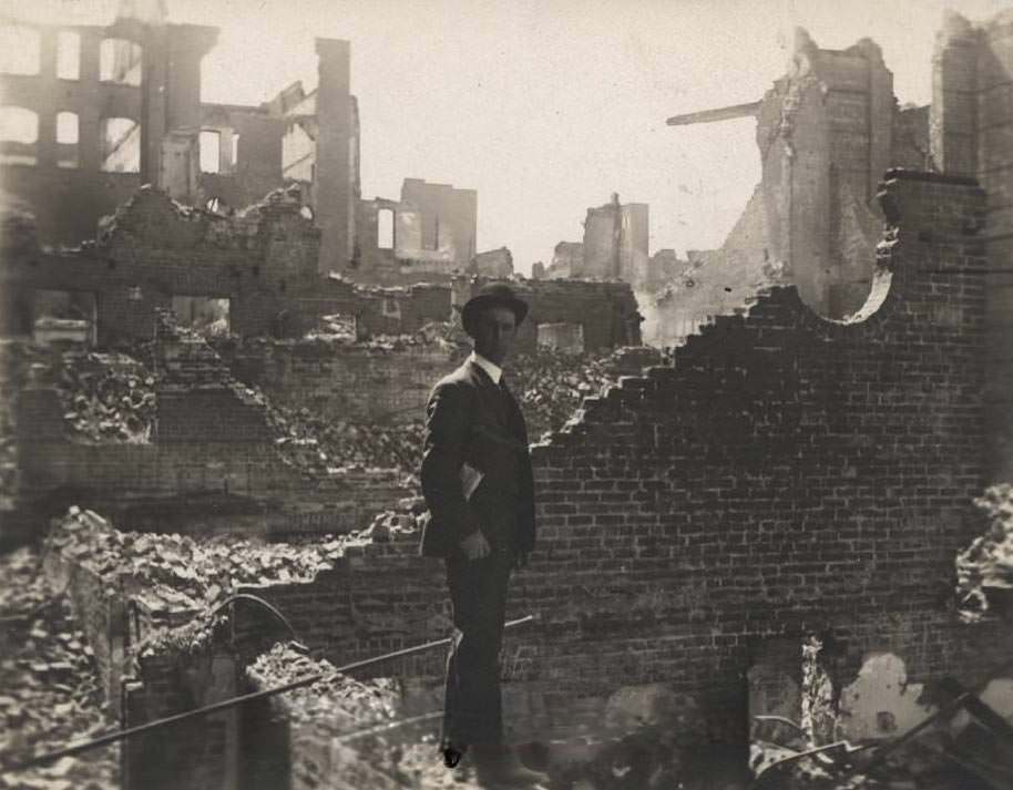 Man looking at photographer while standing on brick rubble, second story of brick, 1906