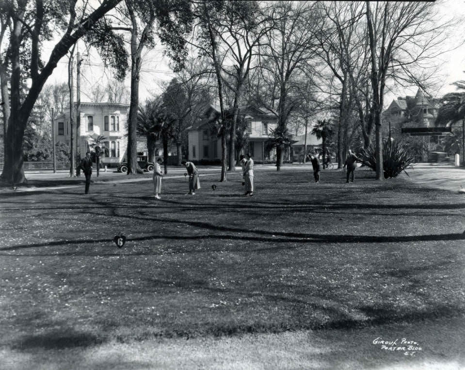 Several men and women play croquet on the lawn of the Vendome Hotel, 1871