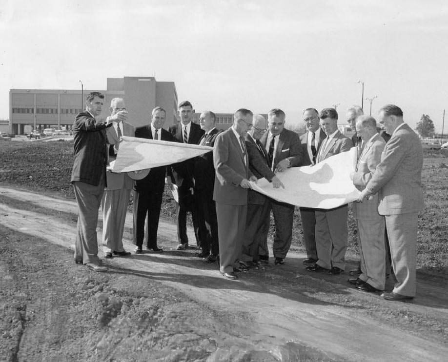 Group of men looking at large plans at construction site, 1959