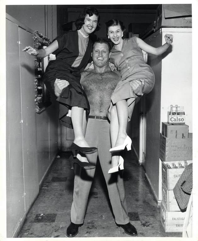 Six-foot five-inch Mike Sharpe lifts lovely ladies Shirlie Montgomery, 1958