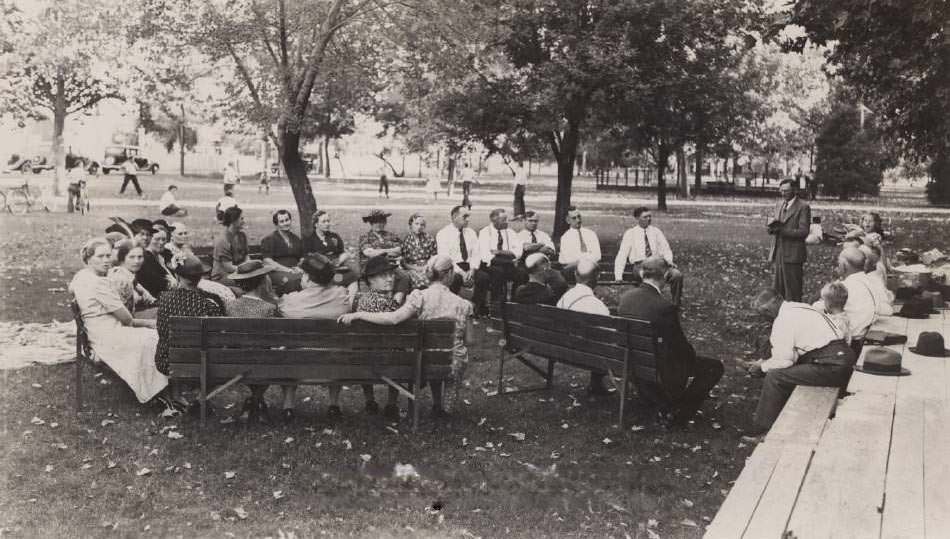 Dr. Reverand Clarence Sands, First Baptist Church in San Jose in front of a group of people sitting on park benches, 1945