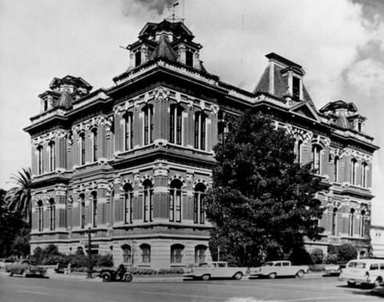 Exterior view of San Jose City Hall with cars and a motorcycle parked alongside it, 1957