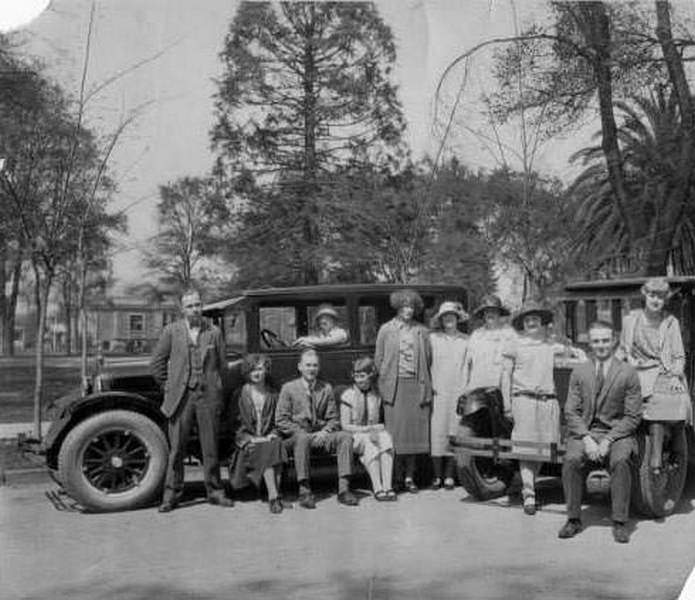 Group of eleven men and women gathered on or near two cars by the campus of San Jose State Teachers College, 1919