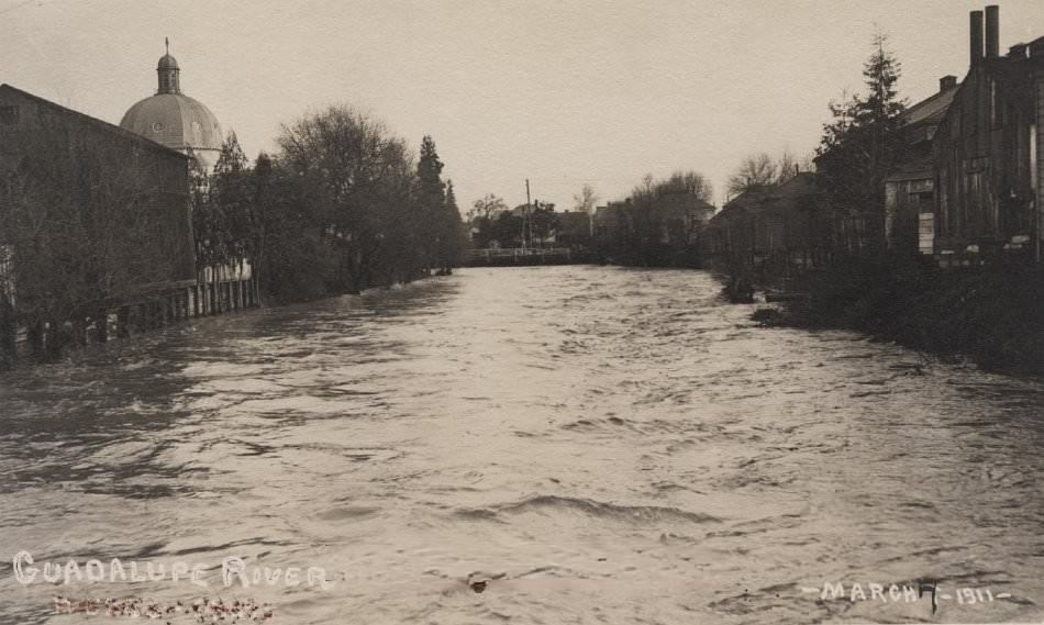View of the Guadalupe River during flood of March 7, 1911 with buildings and Holy Family church dome in the background