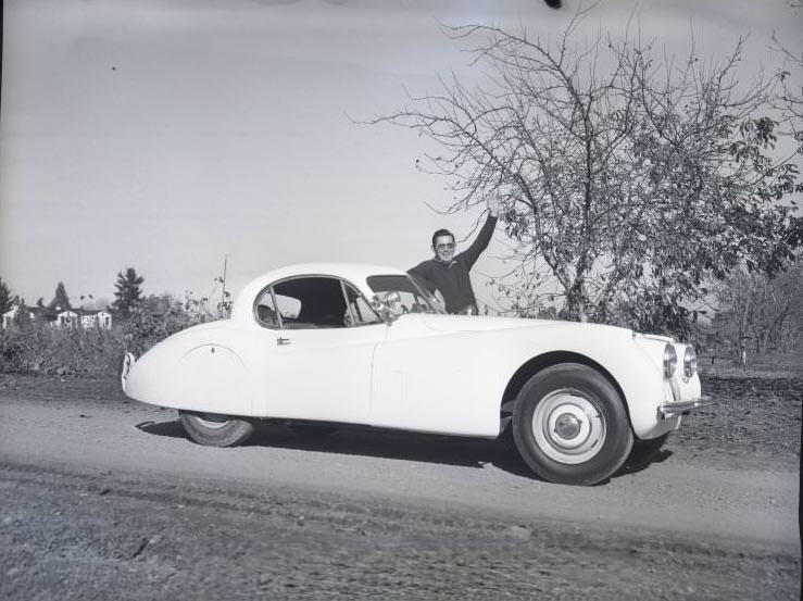 BIll Emerson posing with his jaguar sportscar on a country road, 1954