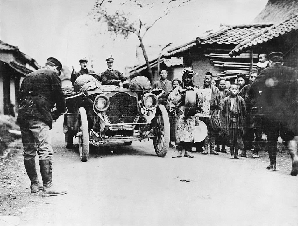 Drivers of the Thomas Flyer, victorious American auto in the 1908 New York to Paris Auto Race, ride with crowds in Manchuria.