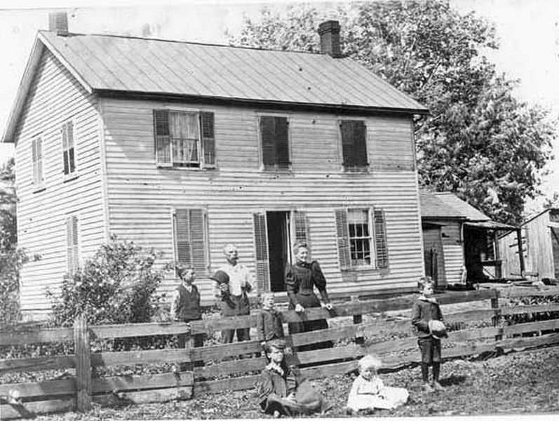 A man and woman stand outside a house with children at the Carty house in Ridgefield, 1890