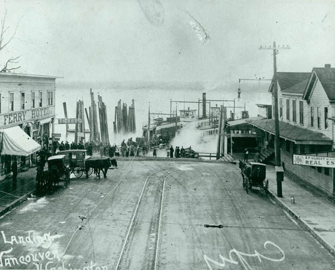 Ferry landing at Vancouver Washington with the Ferry just off the dock with a hotel on the left, and horse drawn carriages and people on the street leading to the landing, 1890s