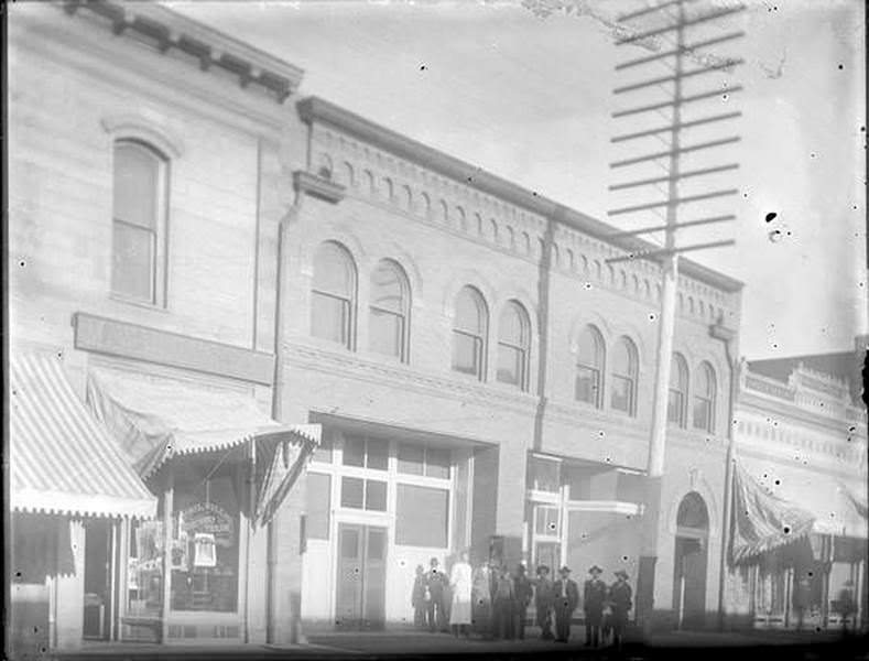 A group of men stand in front of a building housing the Phil Willig Merchant Tailor shop, 1930s