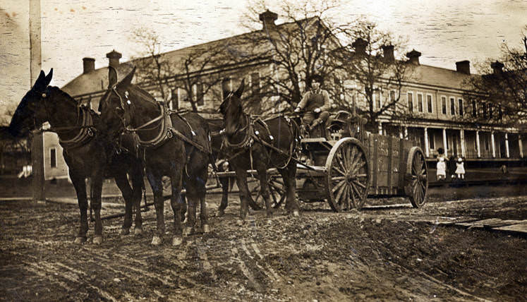 A man with a team of horses and a wagon sit in front of a building at the Vancouver Barracks, 1910