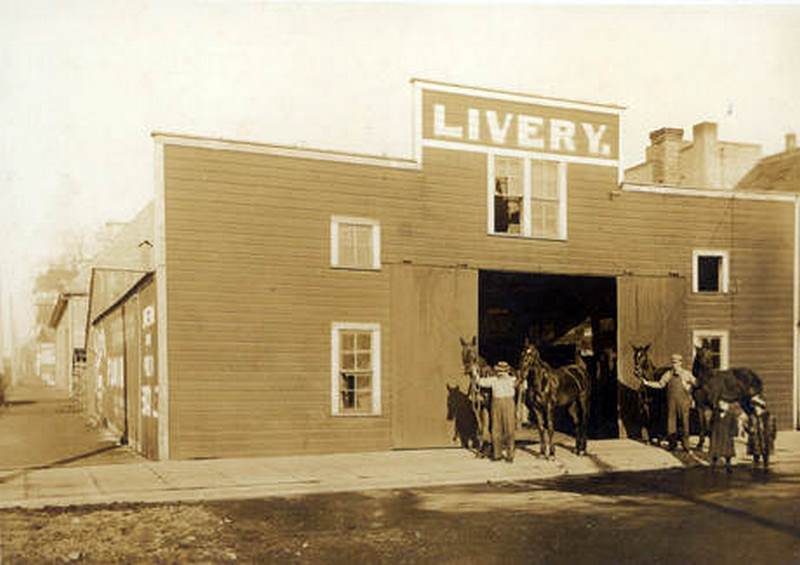 John Crass (in white shirt) walking out horses with a helper at a livery stable located at 214 West 4th Street in Vancouver, 1900s