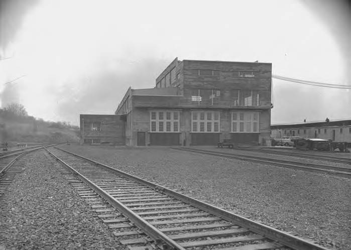 An SP&S diesel shop at a railroad yard with train tracks leading to the shop and a building to the right side of the shop in Vancouver, 1952