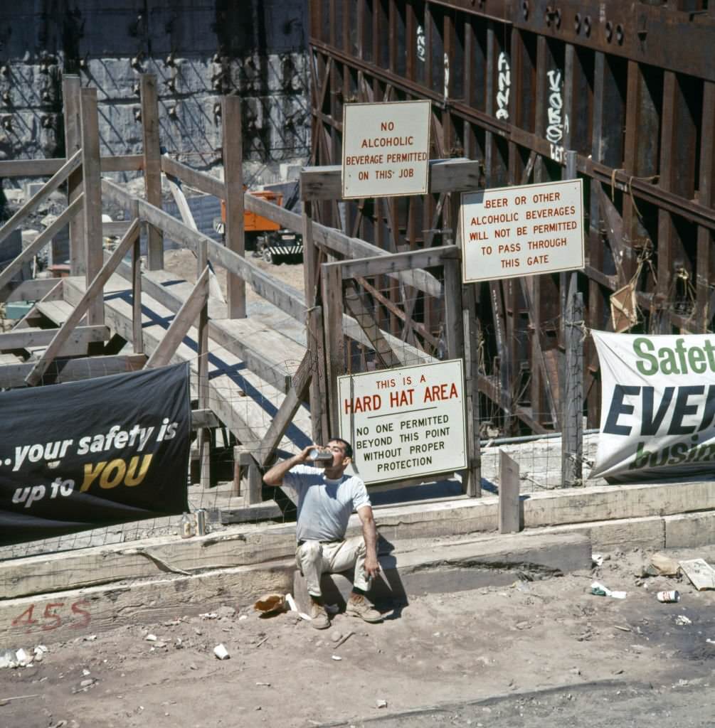 A construction worker as he drinks from am insulated flask, seated on a curb outside the World Trade Center construction site, 1969