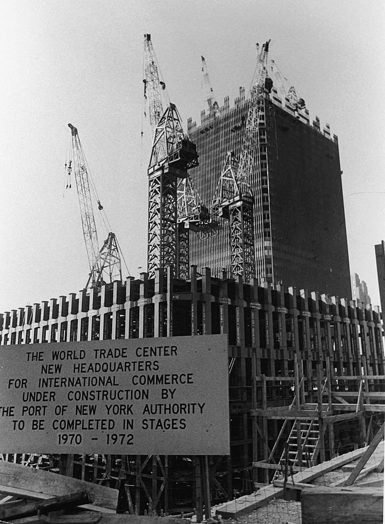 View of the World Trade Center under construction, with a sign announcing the completion schedule, 1969