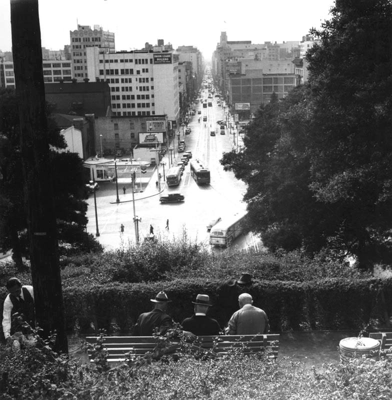 Three men relaxed on a bench overlooking South Hill Street in Los Angeles.