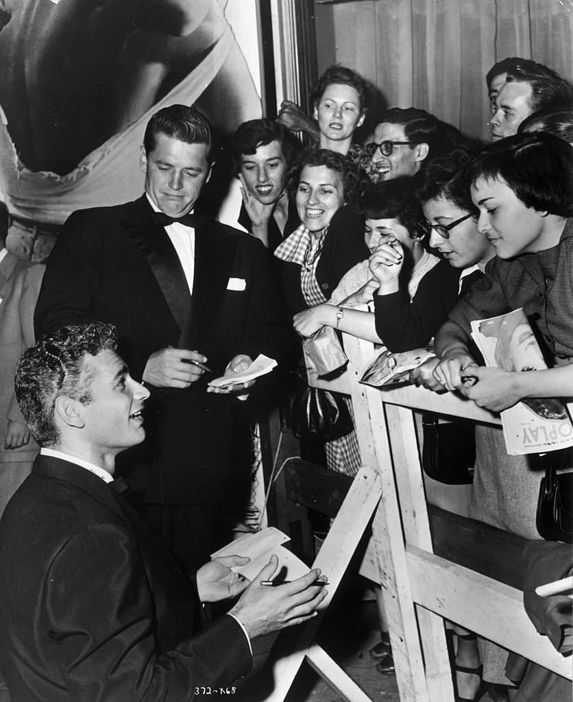 Jeff Chandler (L) and Gordon MacRae sign autographs for smiling fans waiting behind a barrier at the Hollywood premiere of 'Streetcar Named Desire,'.