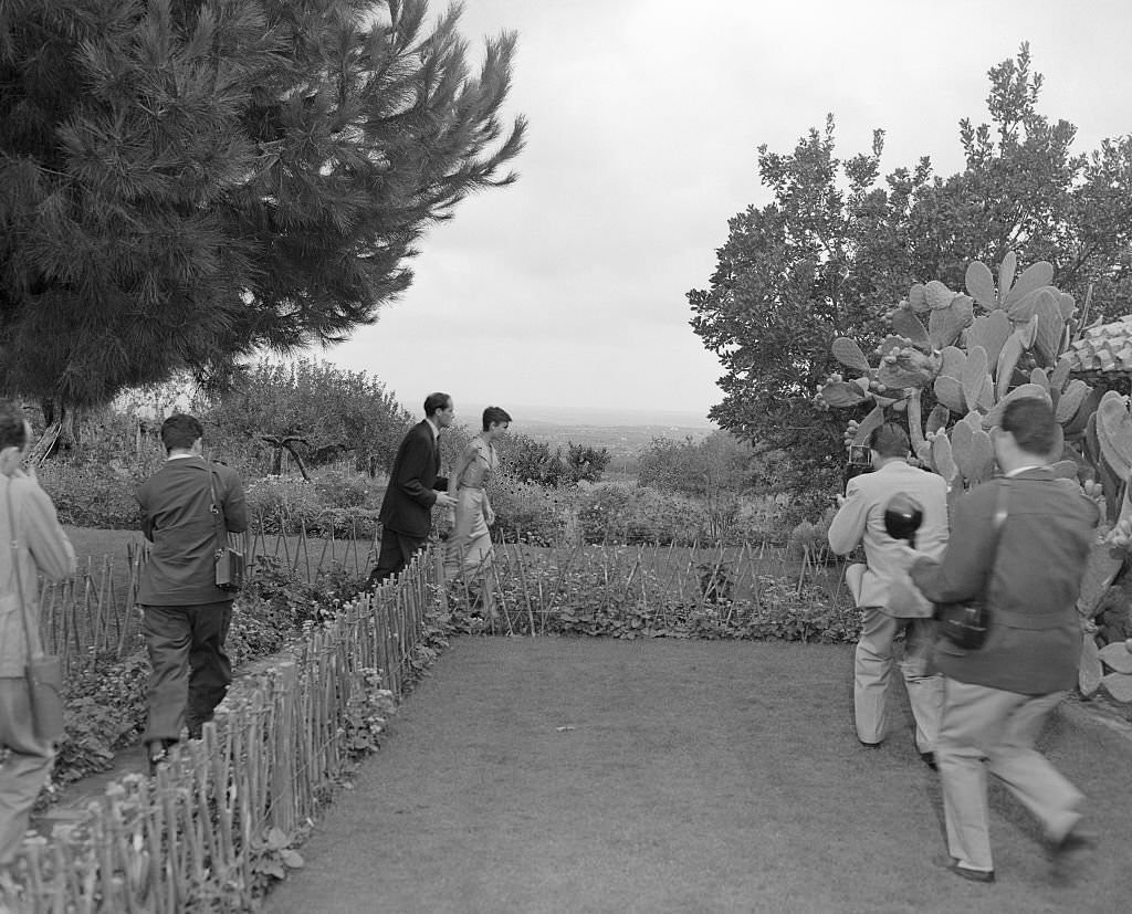 Newlyweds Audrey Hepburn and Mel Ferrer flee photographers on the grounds of the villa near Albano where they are honeymooning.