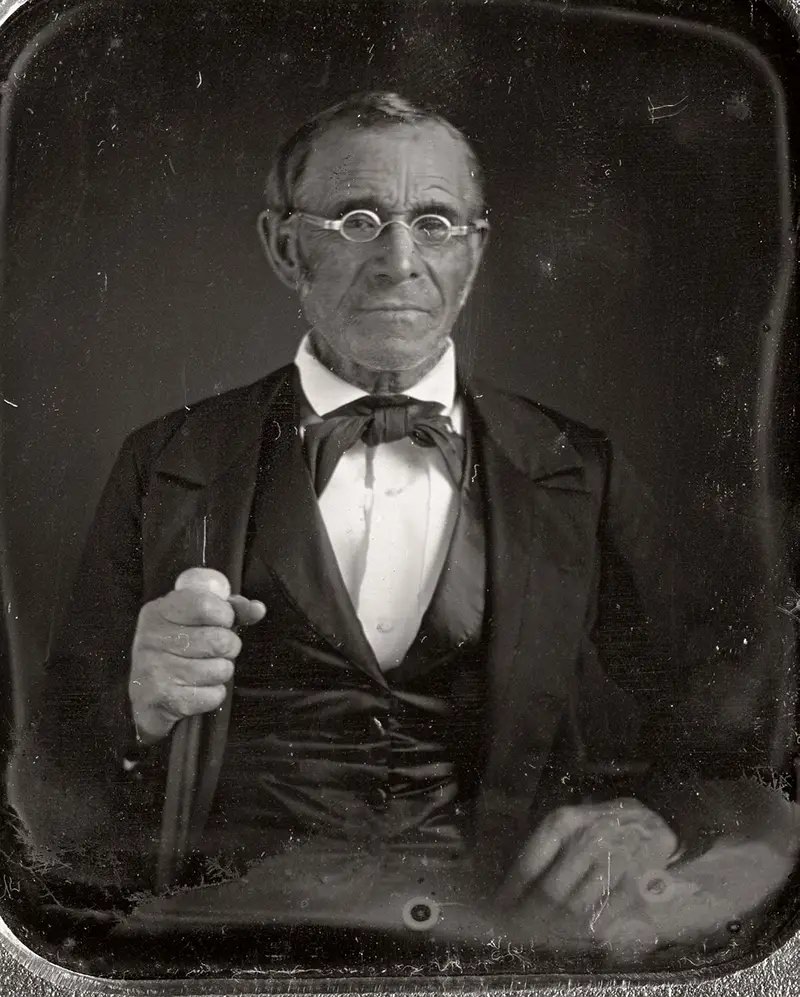 This elderly man is photographed holding a walking cane, 1850.