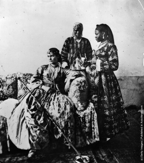 A white lady in crinoline, attended by two women, in a harem in Cairo, 1870