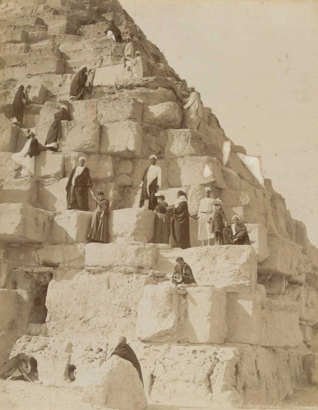 European tourists and local guides climb one of the pyramids at Giza