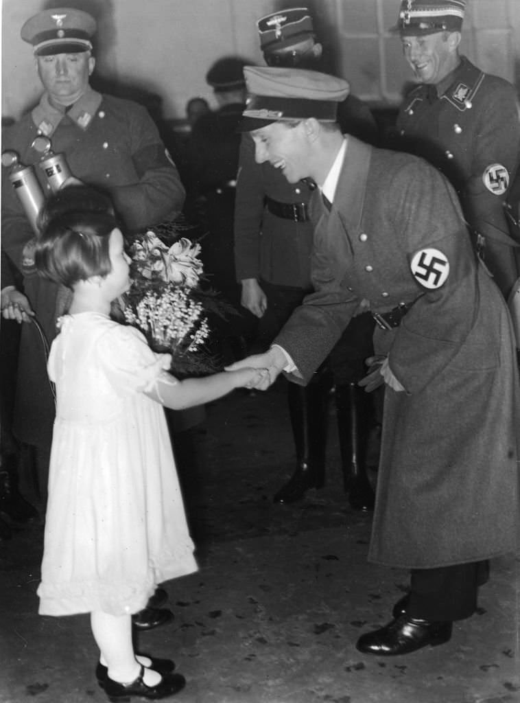 Joseph Goebbels shakes hands with a little girl in a white dress who holds a bouquet of wildflowers, 1930s.