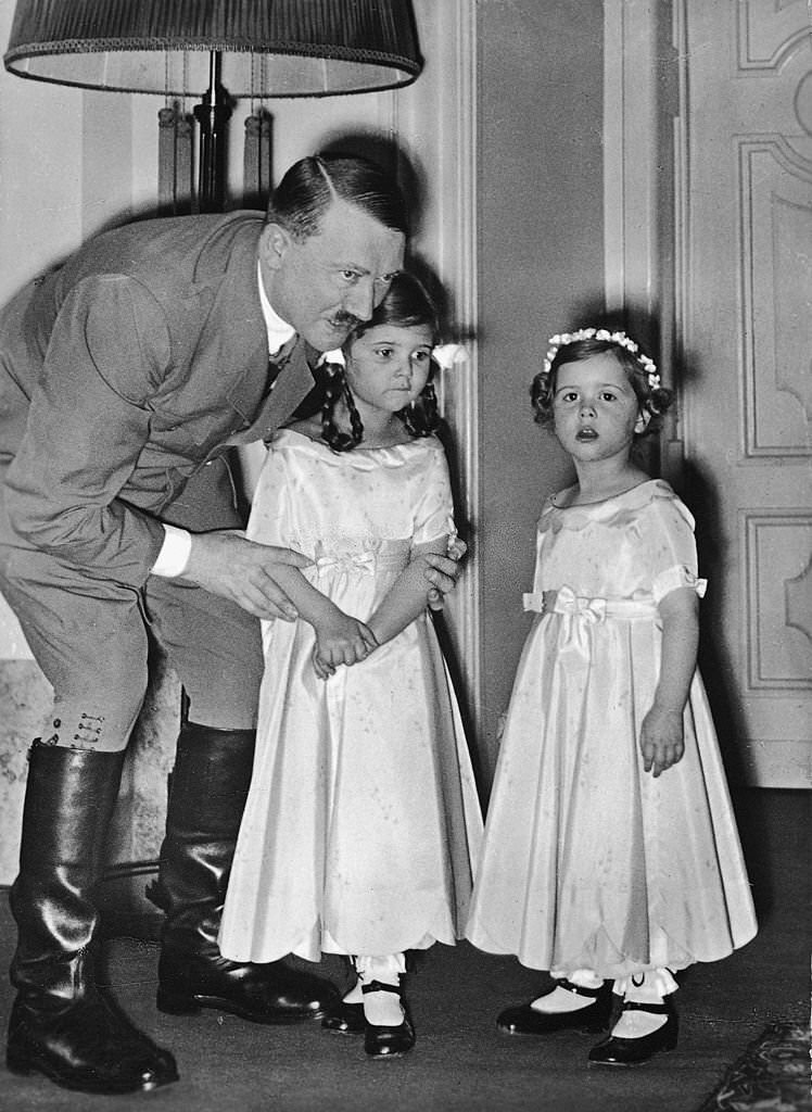 Adolf Hitler adjusts the arms of one of Joseph Goebbels' daughters as they and another Goebbels daughter pose for a photograph, late 1930s.