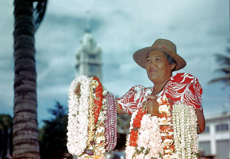 Hawaiian woman selling lei with Aloha Tower in the background, Honolulu Harbor, Oahu, Hawaii