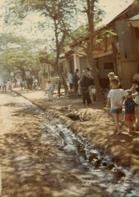 A busy sidewalk scene with stores and the main street in the city of Bồng Sơn in South Vietnam.
