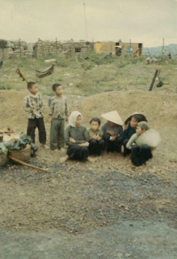 Several Vietnamese women and children, considered prisoners, sitting on the ground near the helicopter landing area of the 2nd Battalion.