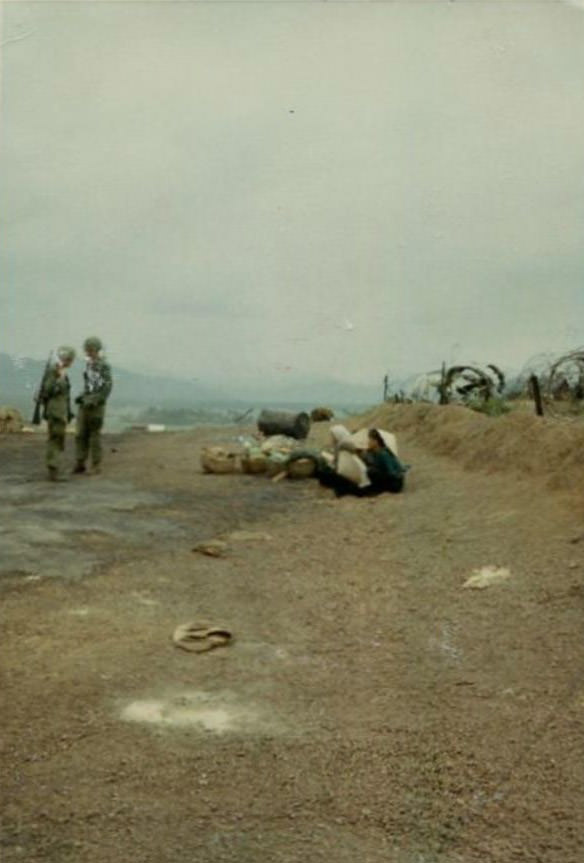 Several Vietnamese women and children, considered prisoners, sitting on the ground near the helicopter landing area of the 2nd Battalion.