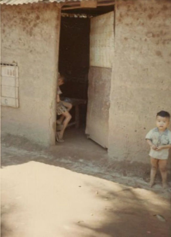 The entrance to an unidentified Vietnamese house with a toddler boy standing outside, somewhere in South Vietnam during the Vietnam War