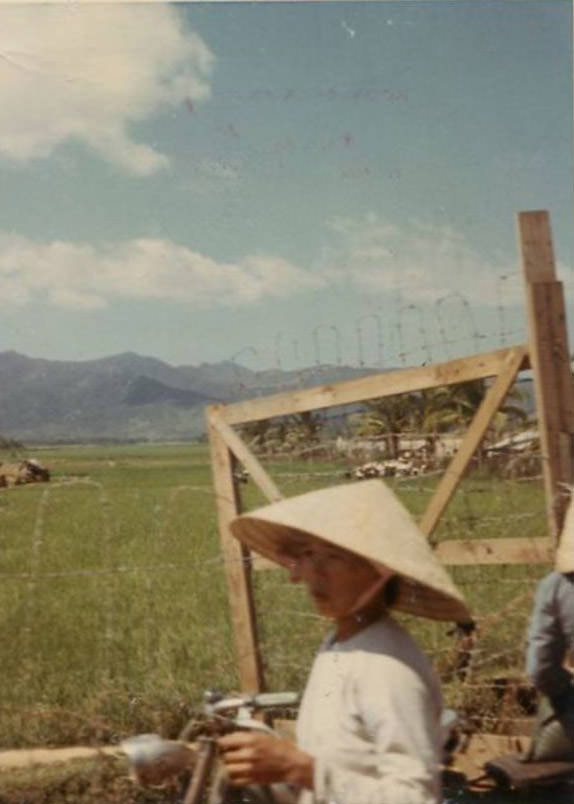 A road somewhere in South Vietnam, looking out over rice paddies and a distant mountain range.