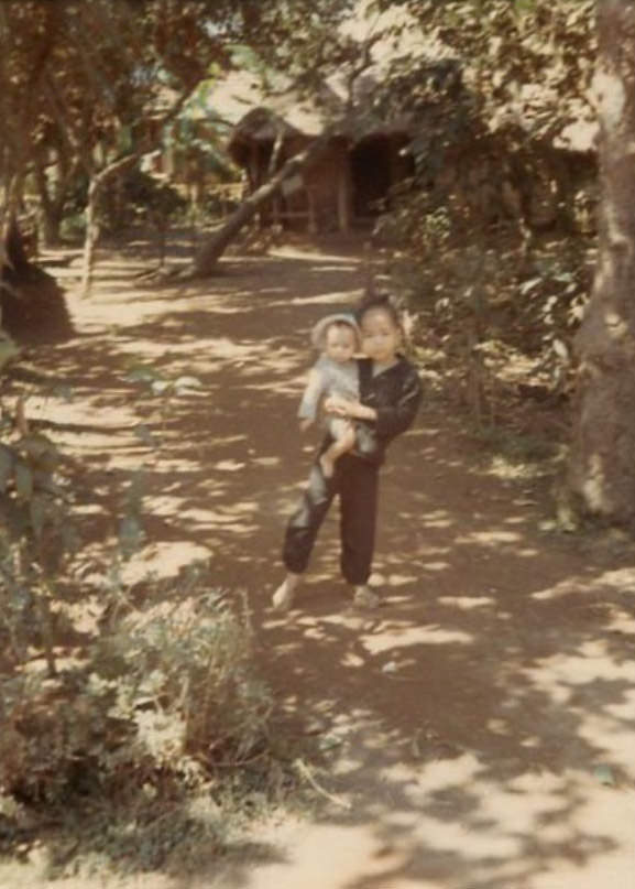 A Vietnamese child holding a toddler outside on a dirt path in an unidentified Vietnamese village somewhere in South Vietnam.