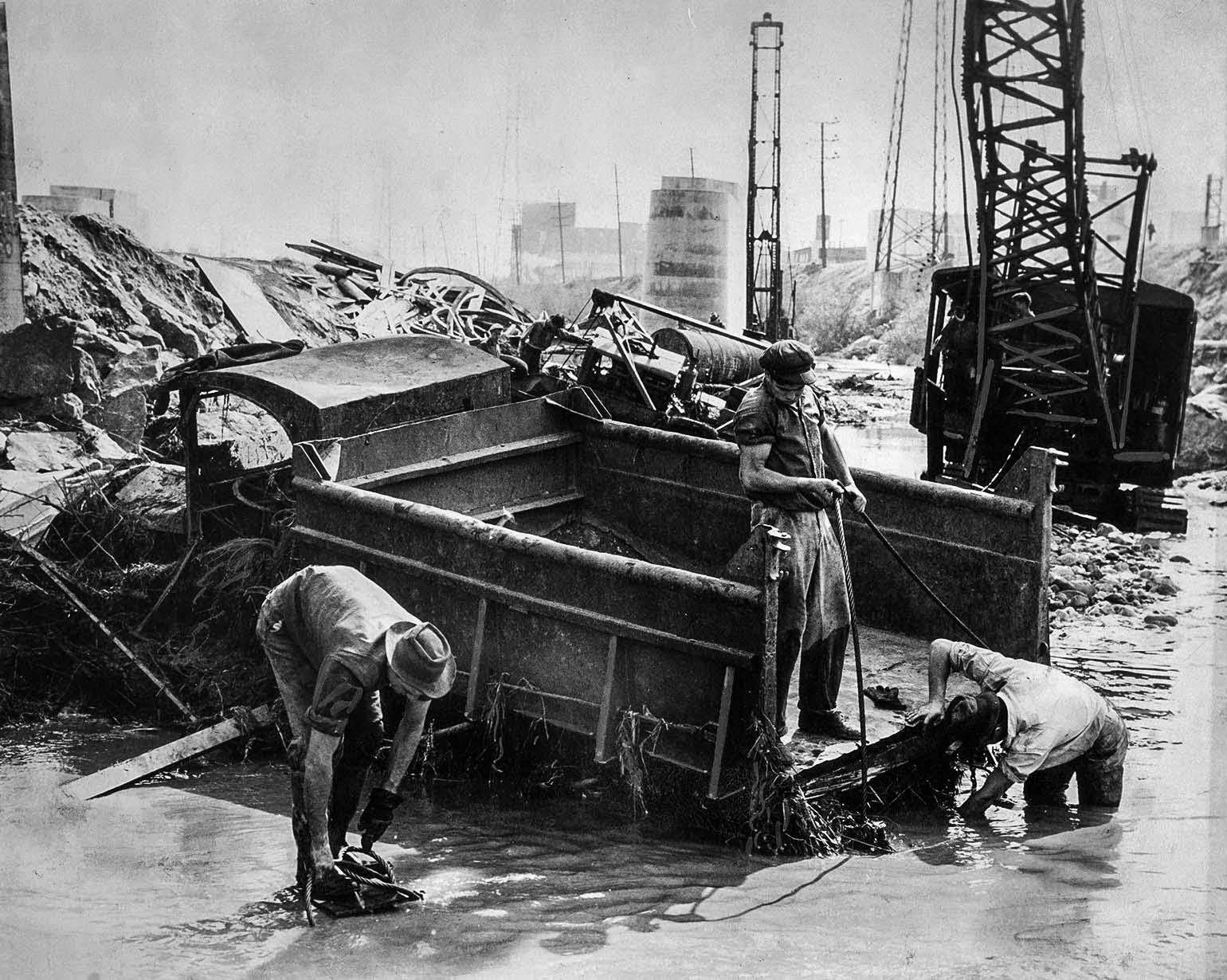 A salvage crew trys to dig out a gravel truck damaged by flooding along the Los Angeles River. The truck was at a construction project to build a railroad crossing for Union Pacific across the river, 1938